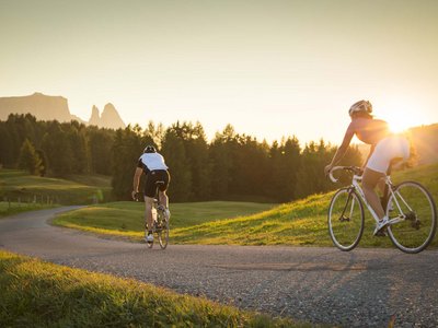 Hotel Schmung: hiking holiday at Alpe di Siusi/Seiser Alm Two cyclists riding on a country road at sunset in the mountains