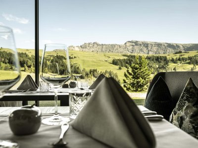 Hotel Schmung – Ihr Hotel auf der Seiser Alm Eleganter Tisch mit Weingläsern vor Panoramafenstern und Bergblick