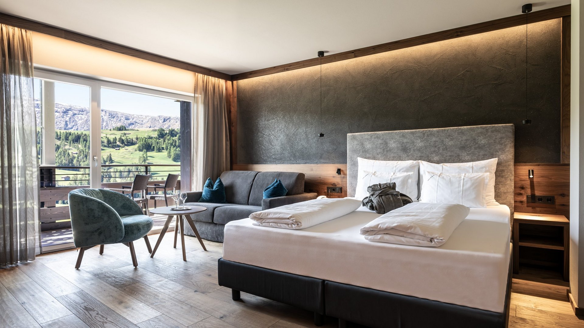 Hotel Schmung – Ihr Hotel auf der Seiser Alm Modernes Hotelzimmer mit Doppelbett, Sofa und Balkon mit Bergblick