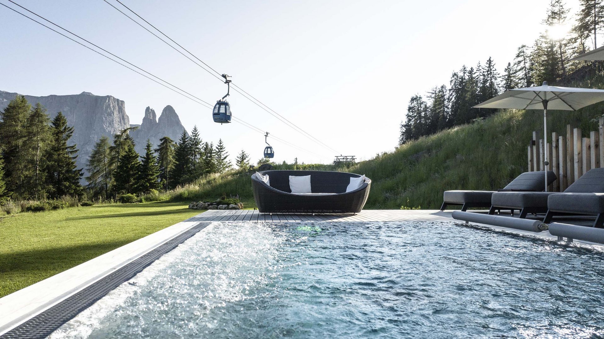 Il nostro hotel con jacuzzi in Alto Adige Piscina con zona relax, lettini e funivia davanti alle montagne