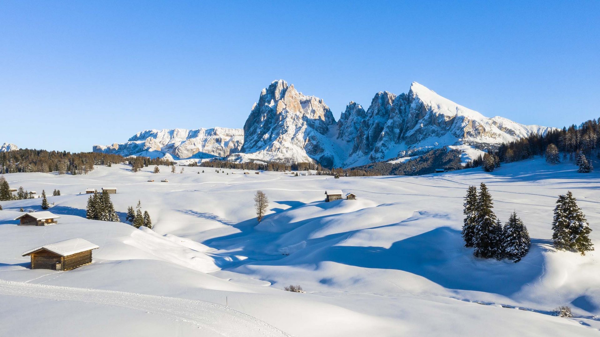 Il programma settimanale dell’Hotel Schmung Prati innevati con baite di legno e montagne al sole in inverno
