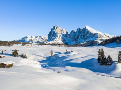 Activities around our hotel in the Dolomites Snow-covered alpine meadows with wooden huts and mountain backdrop in sunny winter