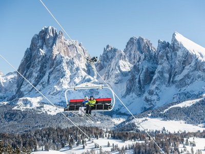 Winterurlaub auf der Seiser Alm imHotel Schmung Zwei Skifahrer auf einem Sessellift vor schneebedeckten Bergen und blauem Himmel