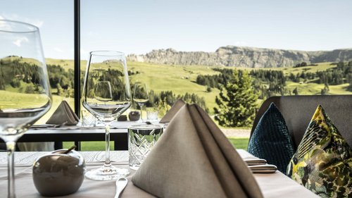 Dolomiti Springdays Tavolo apparecchiato con vista su montagne verdi attraverso la finestra del ristorante