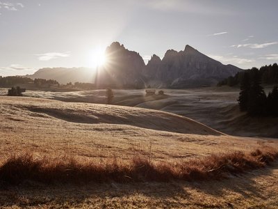 Hotel Schmung: hiking holiday at Alpe di Siusi/Seiser Alm Sunrise over mountains with meadows and small huts