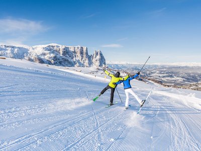Winterurlaub auf der Seiser Alm imHotel Schmung Zwei Skifahrer auf verschneiter Piste mit Bergkulisse und blauem Himmel