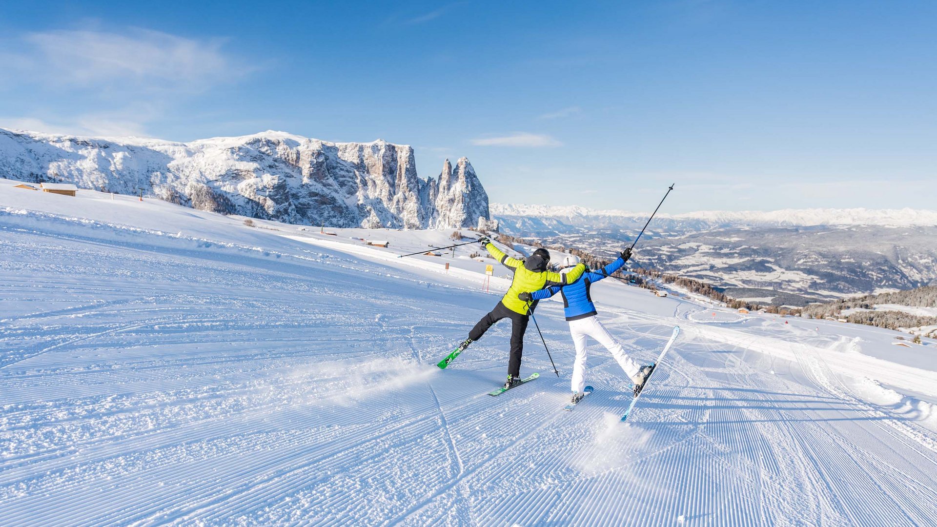 Two skiers on snowy slope with mountain background and clear blue sky