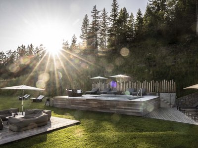 Il nostro hotel con jacuzzi in Alto Adige Giardino soleggiato con area salotto, lettini e piscina di legno davanti al bosco