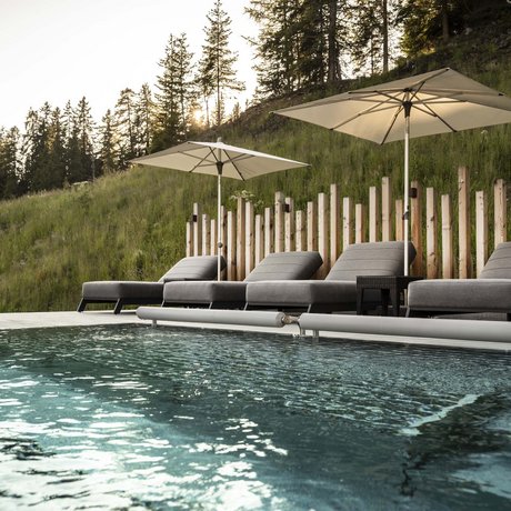 Hotel Schmung: our picture gallery Pool with lounge chairs and umbrellas by forested hill at sunset