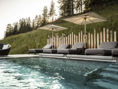 Hotel Schmung: wellness at Alpe di Siusi/Seiser Alm Pool with lounge chairs and umbrellas by forested hill at sunset