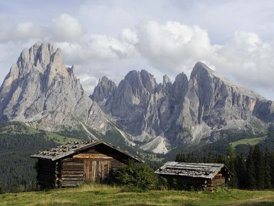 Activities around our hotel in the Dolomites Wooden huts on green meadow with the Dolomites mountains in background