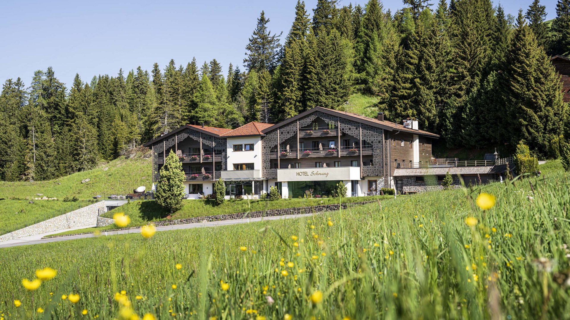 Come arrivare all’Alpe di Siusi? Hotel Schunng in un prato verde davanti a una foresta