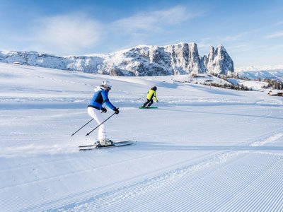 Winterurlaub auf der Seiser Alm imHotel Schmung Zwei Skifahrer auf einer präparierten Piste mit verschneiten Bergen im Hintergrund