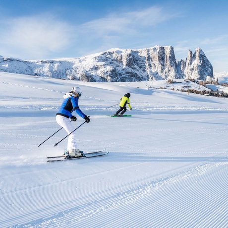 Hotel Schmung: our picture gallery Two skiers on a groomed slope with snowy mountains in the background