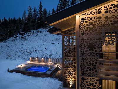 Il nostro hotel con jacuzzi in Alto Adige Vasca idromassaggio illuminata accanto a casa in legno decorata in montagna innevata di notte