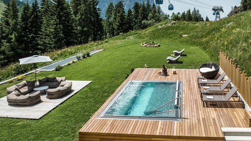 Dolomiti Springdays Area piscina con lettini e funivia su prato verde tra le montagne d'estate