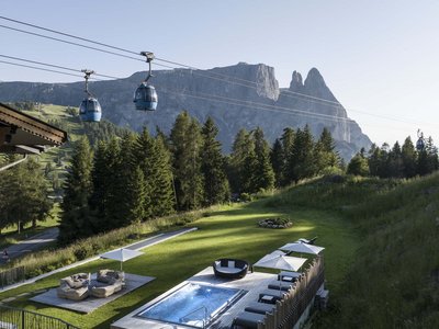 Hotel Schmung – Ihr Hotel auf der Seiser Alm Berglandschaft mit Sessellift, Terrasse und Garten mit Pool und Sitzbereichen