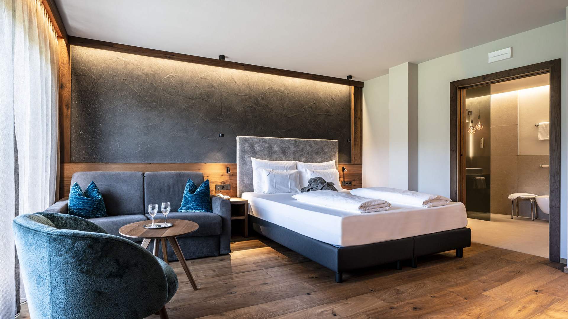 Hotel Schmung – Ihr Hotel auf der Seiser Alm Modernes Hotelzimmer mit Doppelbett, Sofa und Badezimmer