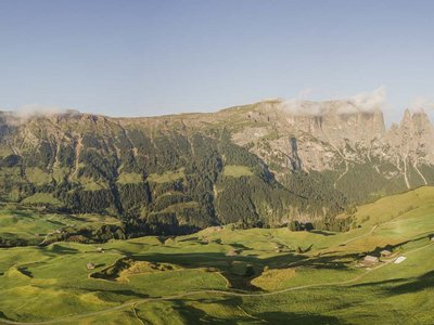 Hotel Schmung: hiking holiday at Alpe di Siusi/Seiser Alm Panoramic view of green hills, mountains, and scattered houses under clear sky
