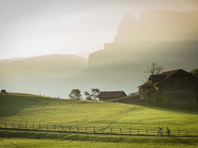 Hotel Schmung: hiking holiday at Alpe di Siusi/Seiser Alm Cyclists riding on path beside farmhouse in sunlit mountain landscape