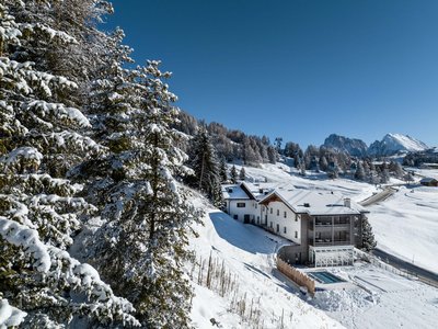 Hotel Schmung: wellness at Alpe di Siusi/Seiser Alm Snowy alpine landscape with hotel, pine trees, and mountain cable cars