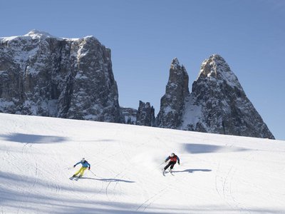 Winterurlaub auf der Seiser Alm imHotel Schmung Zwei Skifahrer vor schneebedeckten Felsen und klarem Himmel