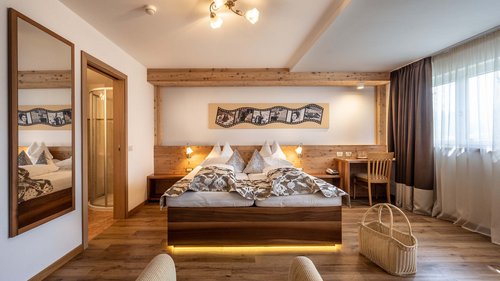 Dolomiti Springdays Camera d'hotel luminosa con letto matrimoniale, pavimento in legno e finestra con tende