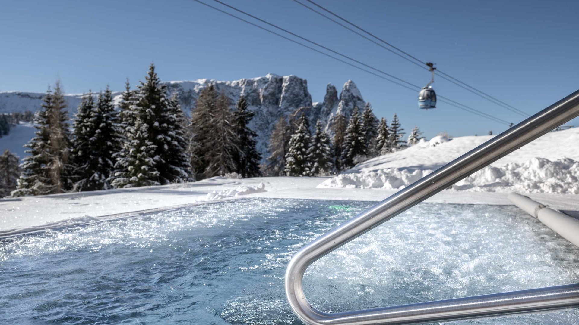 Whirlpool in verschneiter Berglandschaft mit Seilbahn und klar blauem Himmel