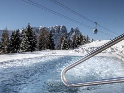 Hotel Schmung: wellness at Alpe di Siusi/Seiser Alm Hot tub in snowy mountain landscape with cable car and clear blue sky