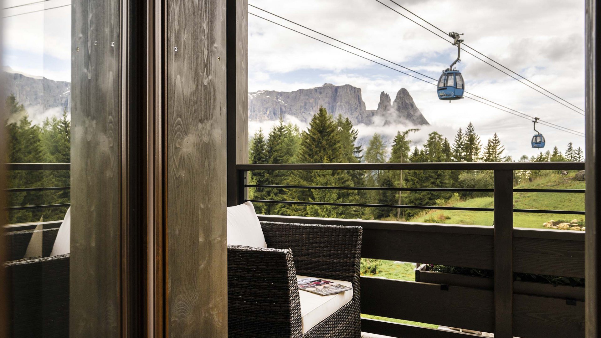 Ihre Unterkunft auf der Seiser Alm Balkon mit Korbsessel, Bergblick und Seilbahn-Gondeln in den Alpen