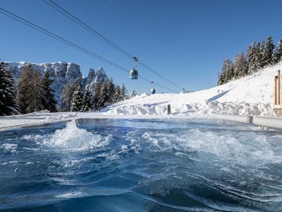 Hotel Schmung: wellness at Alpe di Siusi/Seiser Alm Hot tub with mountains, snow-covered trees and cable cars under clear sky