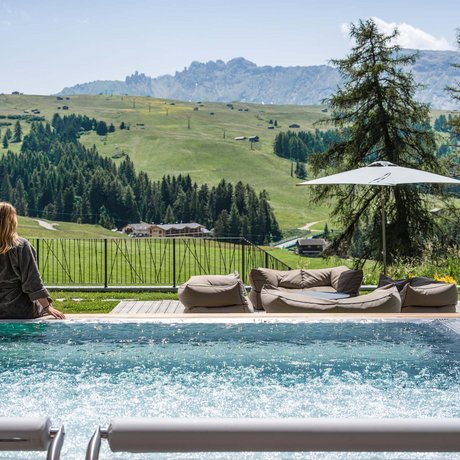 Hotel Schmung: our picture gallery Woman relaxing by pool with mountain view and outdoor seating area